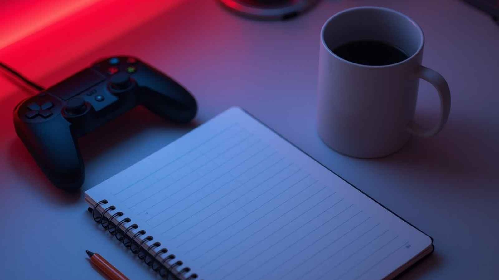 Cozy gaming desk with a blank notebook, controller, and mug in soft LED light.